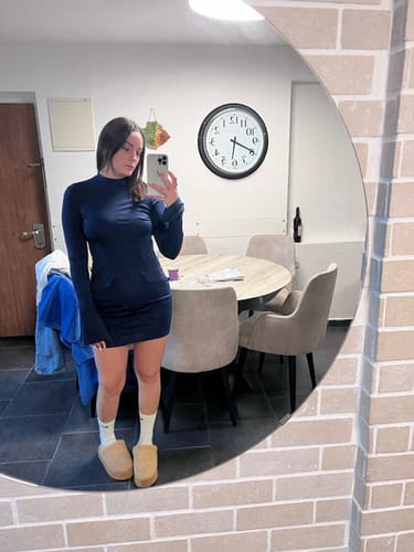 Frau im blauen Kleid macht Selfie im Spiegel; modern eingerichtetes Esszimmer im Hintergrund