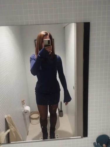 Frau im blauen Kleid macht Spiegelselfie im modernen Badezimmer mit weißen Fliesen.